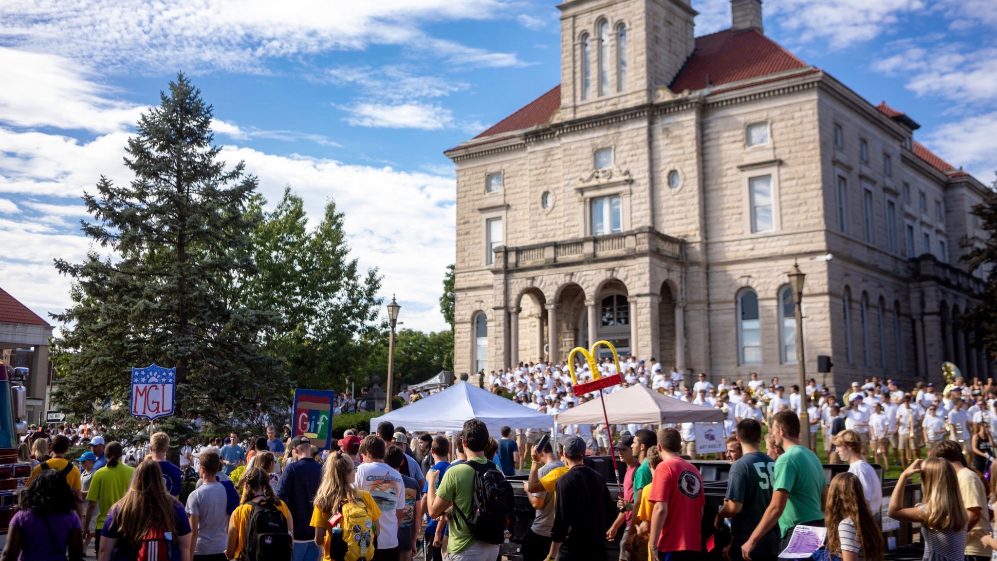 A crowd of students in front of the courthouse, watching the James Madison University marching band perform on the lawn.