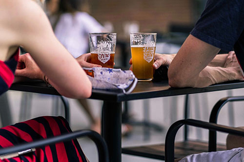 A close-up view of two people sitting at a table outside with two beer glasses between them.