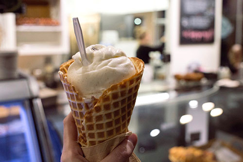 A hand holding an ice cream cone with vanilla ice cream inside.